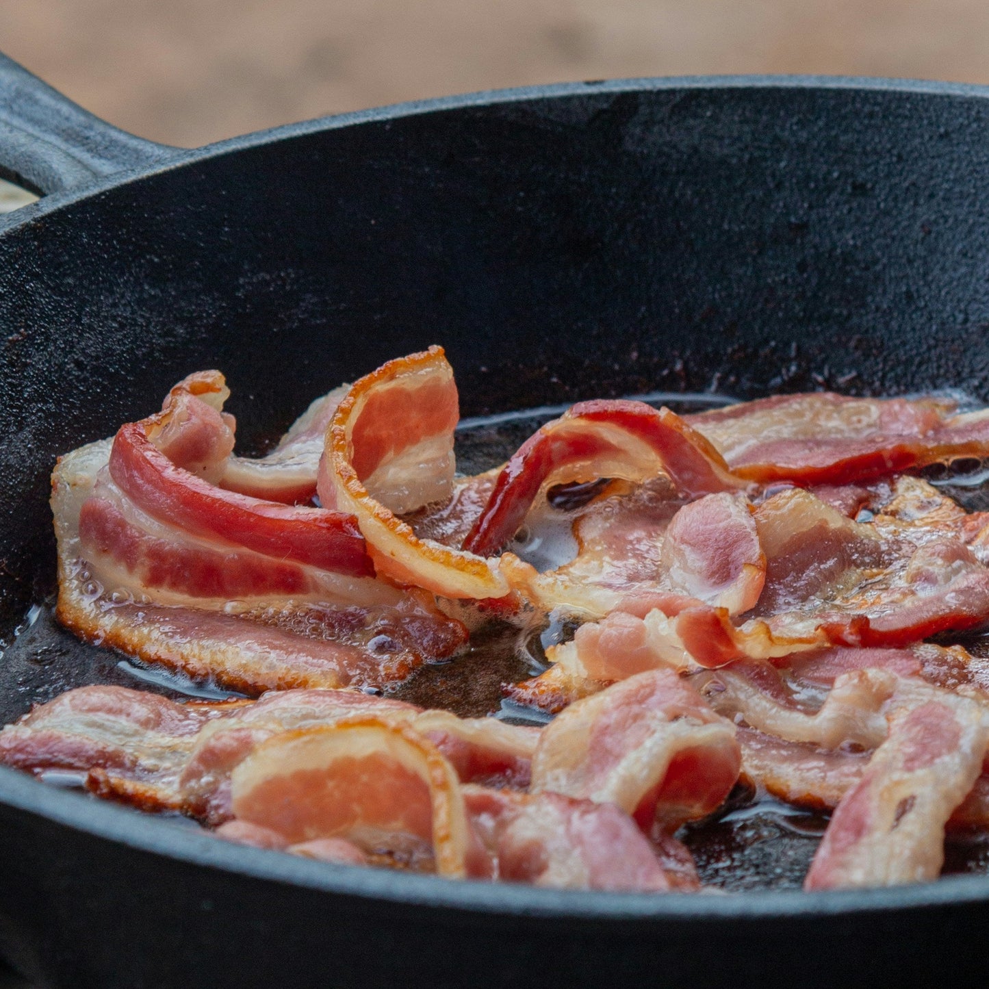 Bacon frying in a black cast iron skillet on a grill.