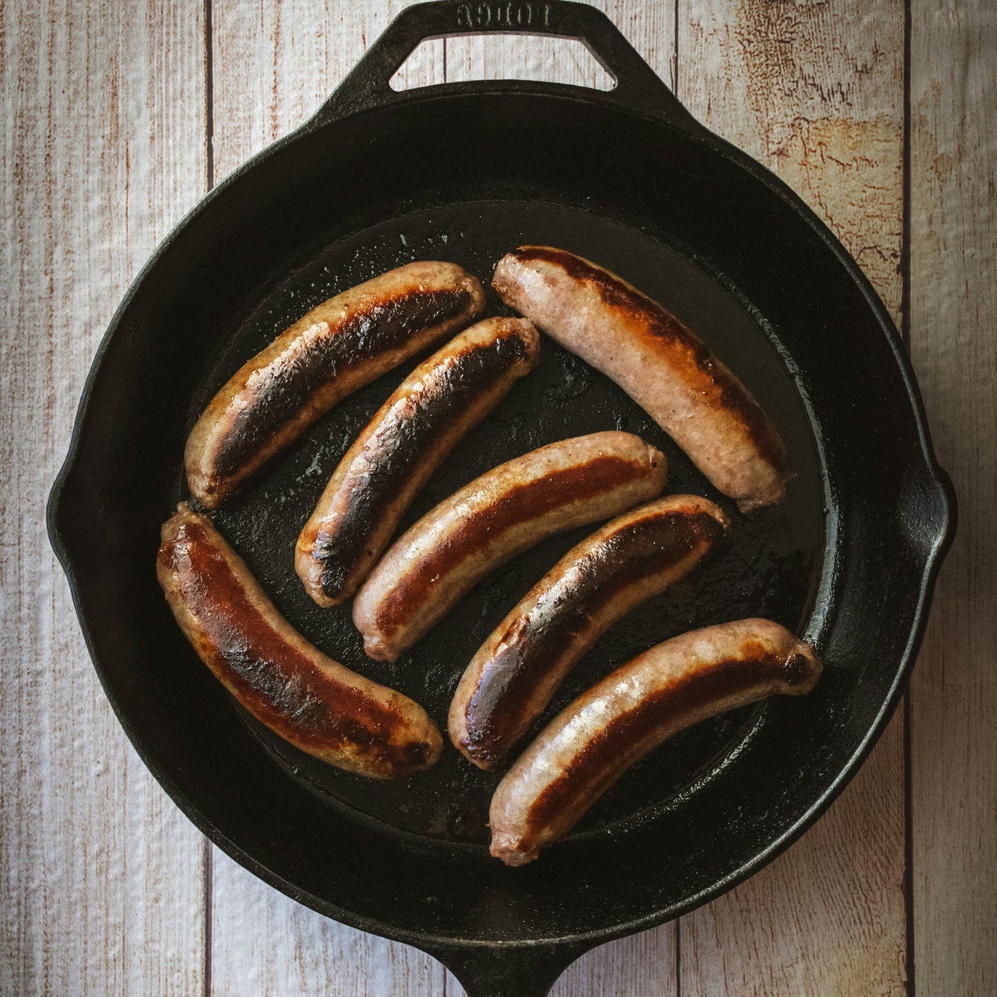 Sausages cooking in a cast iron skillet on a wooden surface