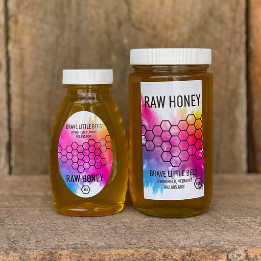Two jars of raw honey from Brave Little Bees on a wooden surface